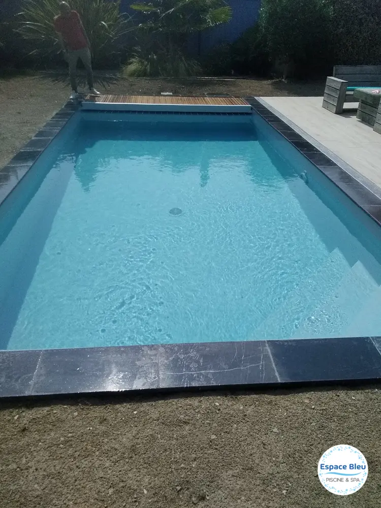Piscine rectangulaire avec margelle sombre et jardin