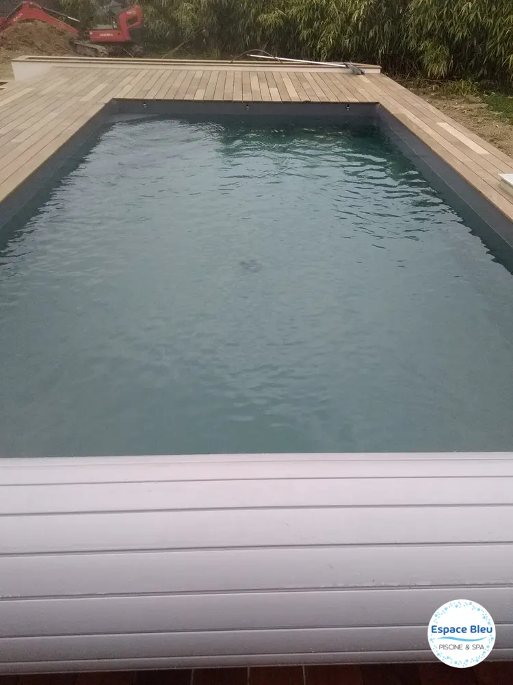 Piscine à eau sombre avec volet gris et terrasse bois