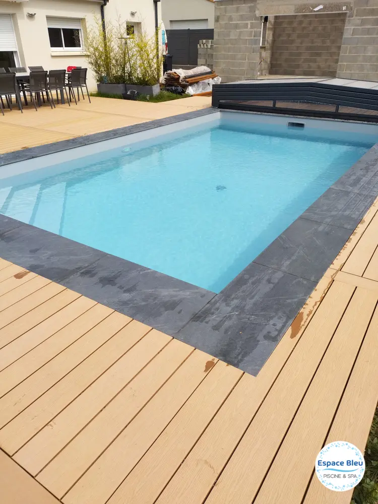 Piscine à eau turquoise, margelle sombre et terrasse bois