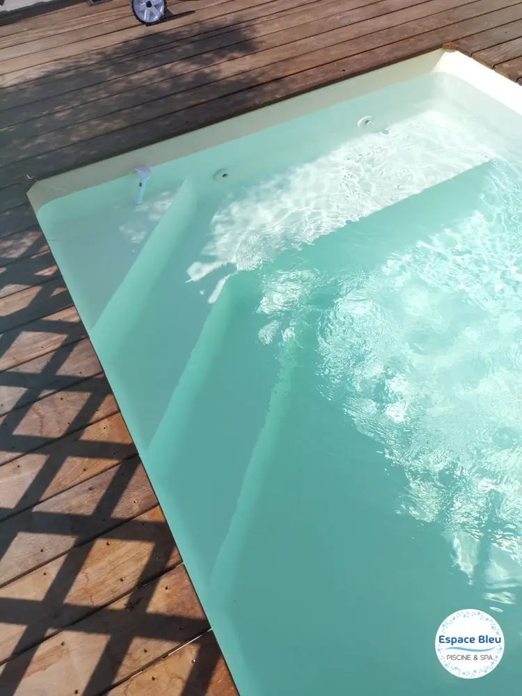 Escalier d’une piscine à eau turquoise, terrasse bois