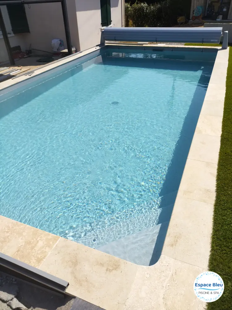 Piscine turquoise avec volet et plage en pierre