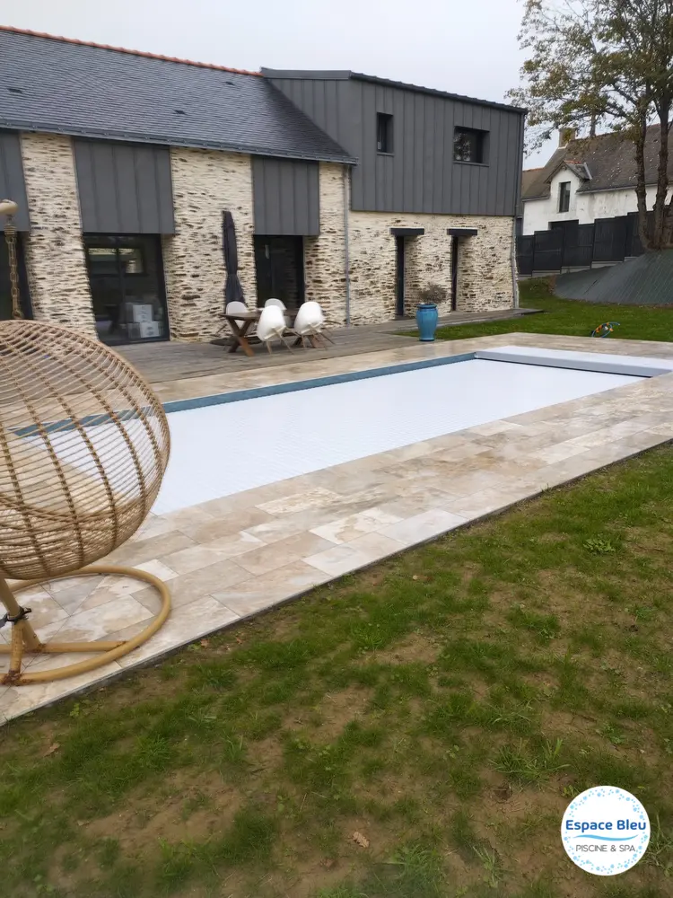 Piscine avec volet blanc devant une maison en pierre