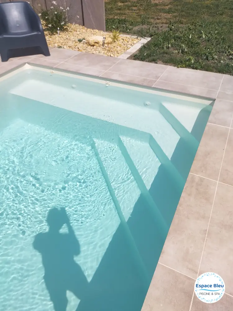 Escalier d’une piscine à eau claire et plage en pierre
