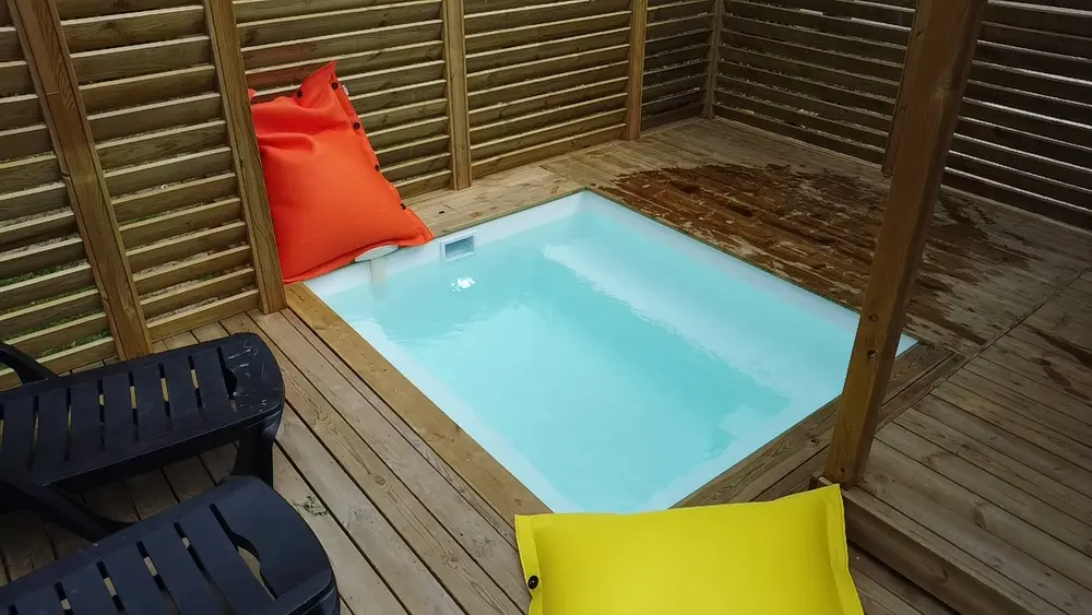 Pool Party installée sur une terrasse bois, avec pouf et coussins colorés